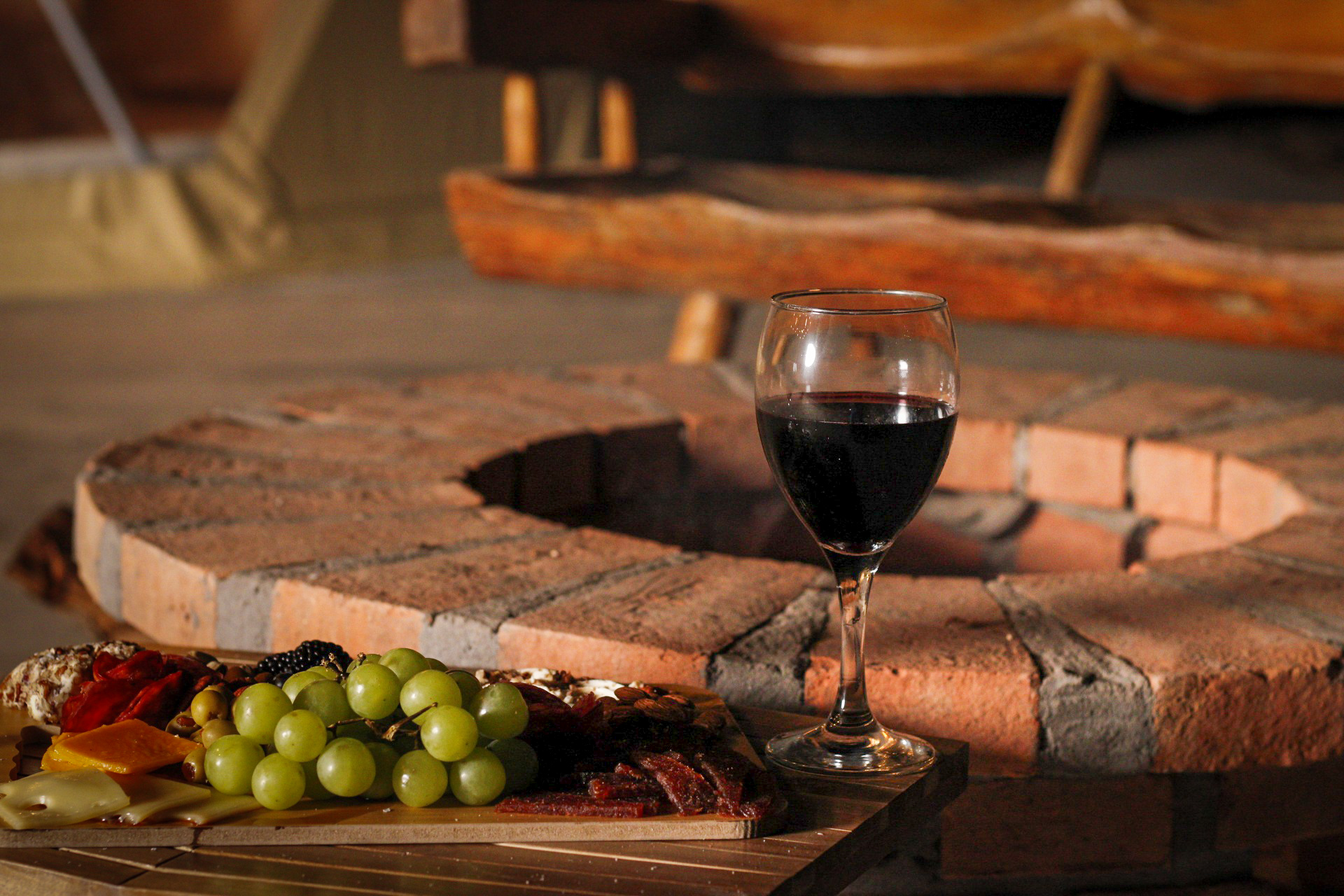 Tabla de charcutería con copa de vino junto a la fogata