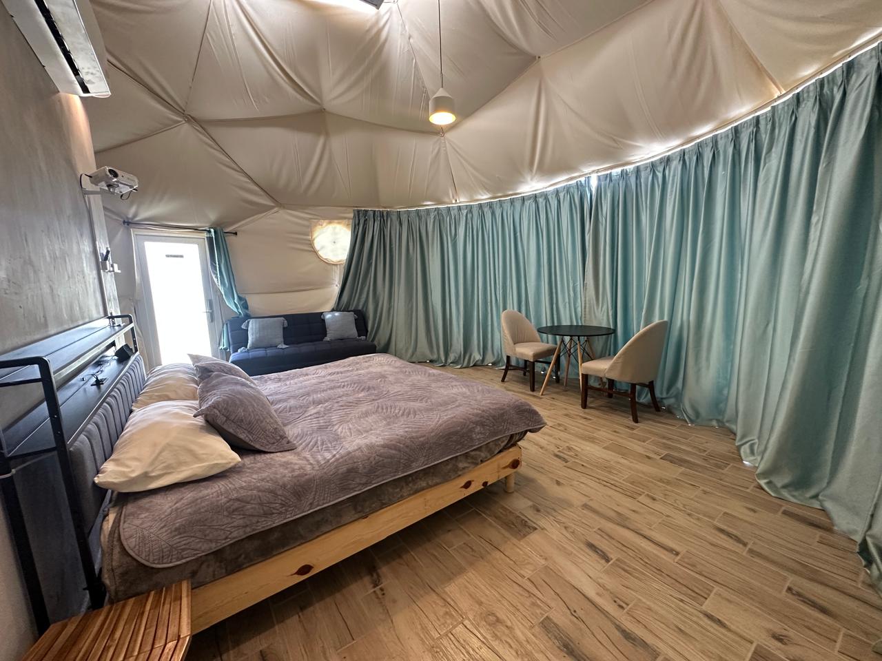 Interior del domo geodésico con cama King Size, sofá cama y proyector en Parque Santa Julia
