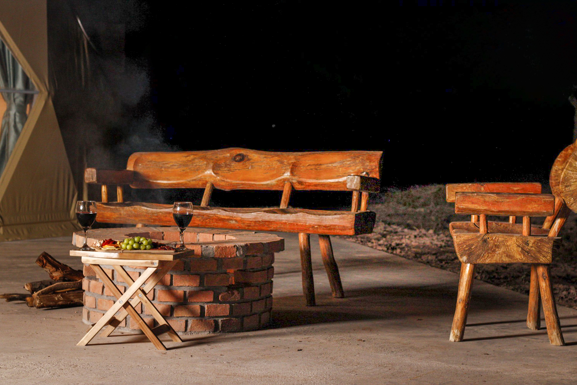 Área de fogata con mobiliario rústico de madera y copa de vino